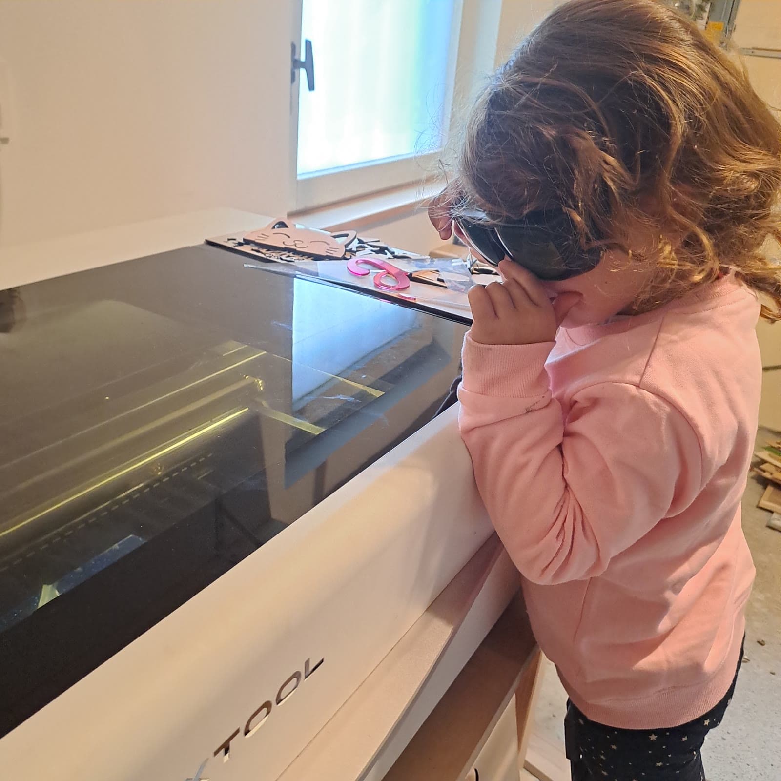 La fille d'Orianne, lunettes de protection sur les yeux, regarde la découpeuse laser xTool de l'atelier